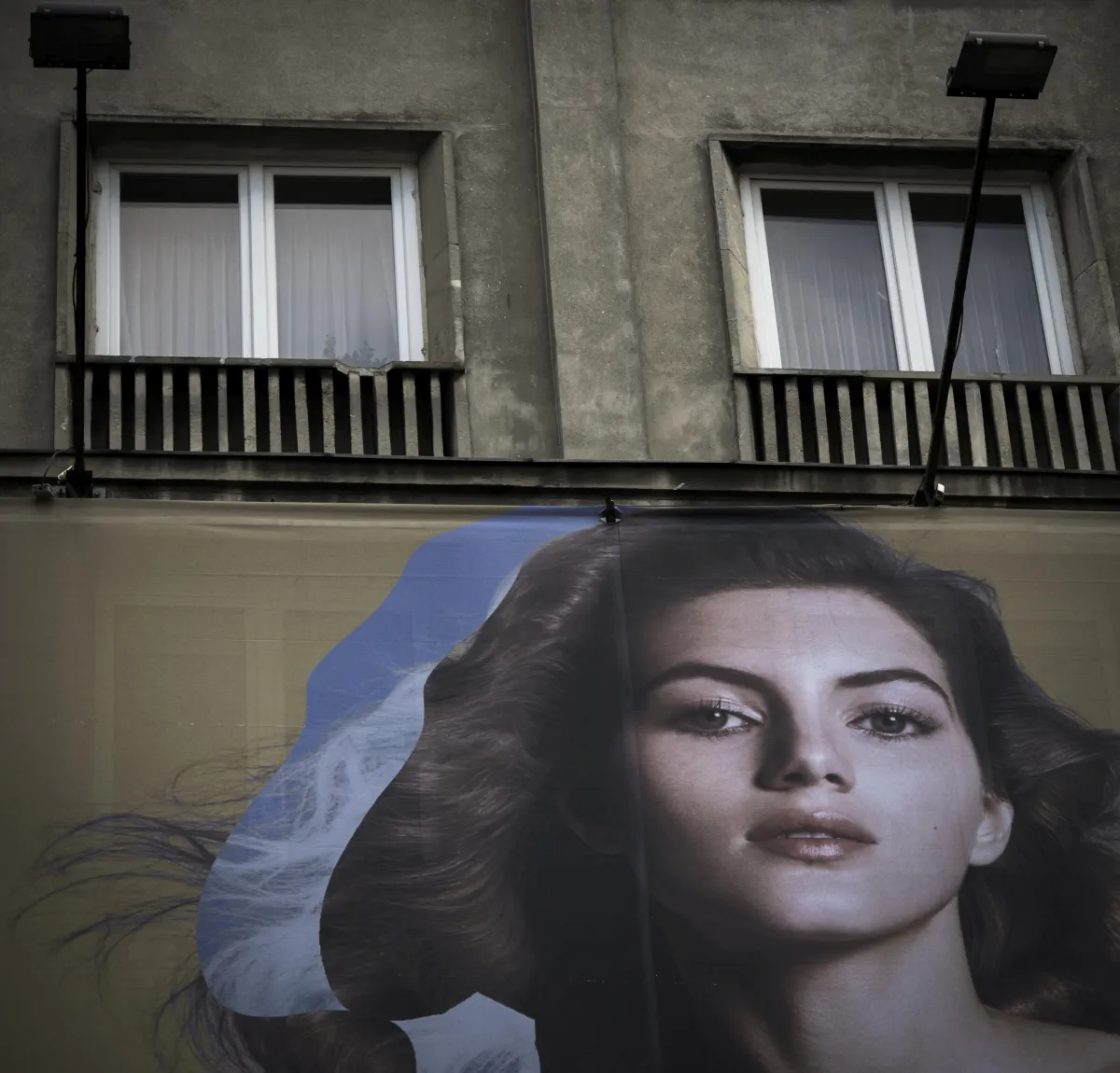 Billboard portrait beneath two apartment windows and balcony shadows
